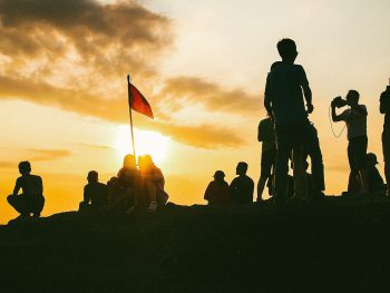 Een groep mensen die samenkomt rondom een vlag bij zonsondergang.