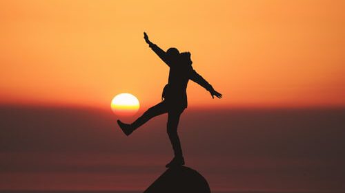 Een persoon die balanceert op een rots, met een ondergaande zon op de achtergrond.